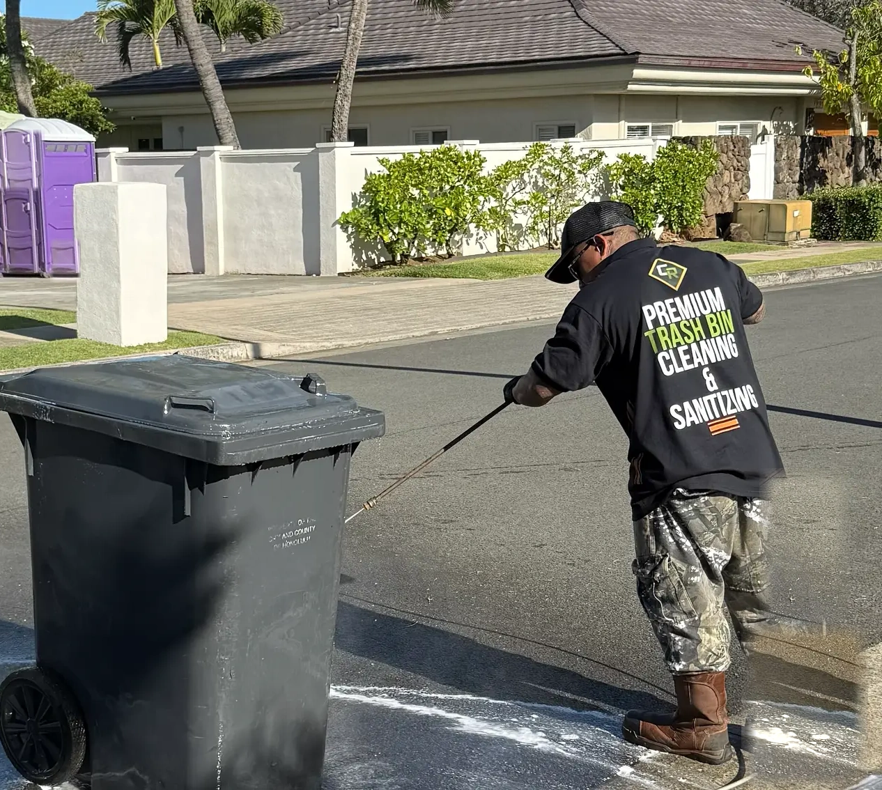 Clean Route Systems technician pressure-washing a curbside trash bin on a residential Oʻahu street